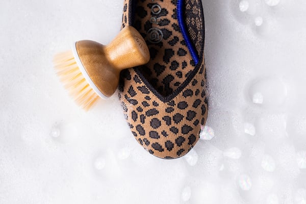 Leopard-print shoe and cleaning brush styled against soap bubbles