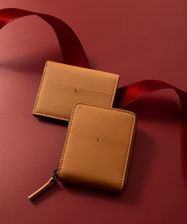 Tan leather accessories photographed against a burgundy background with ribbon